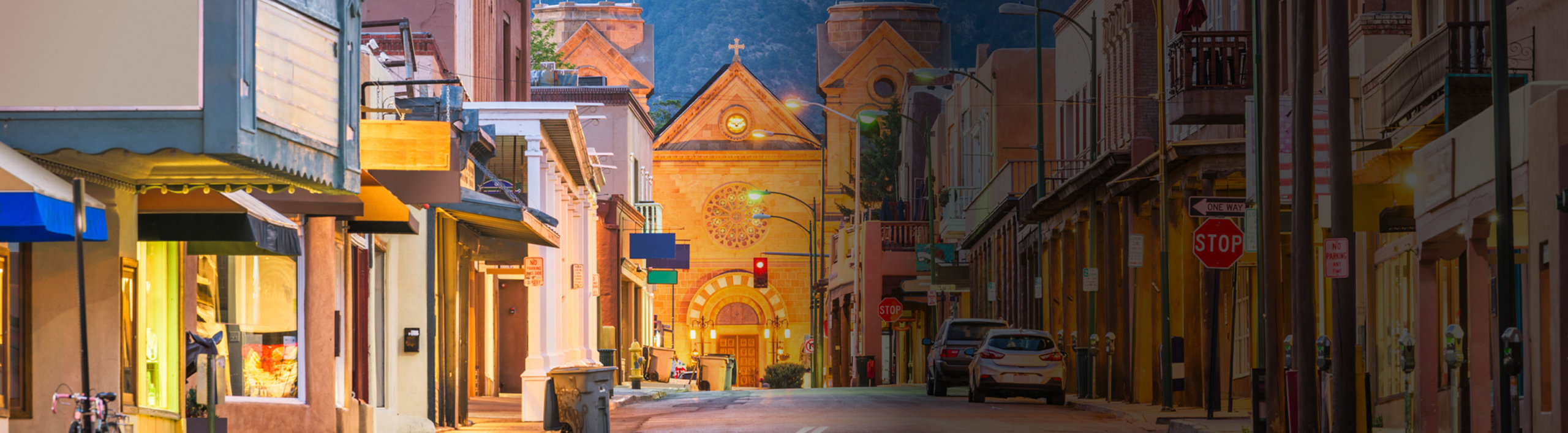 Narrow street with colorful shopfronts leading to a lit historic church in a cozy evening setting.