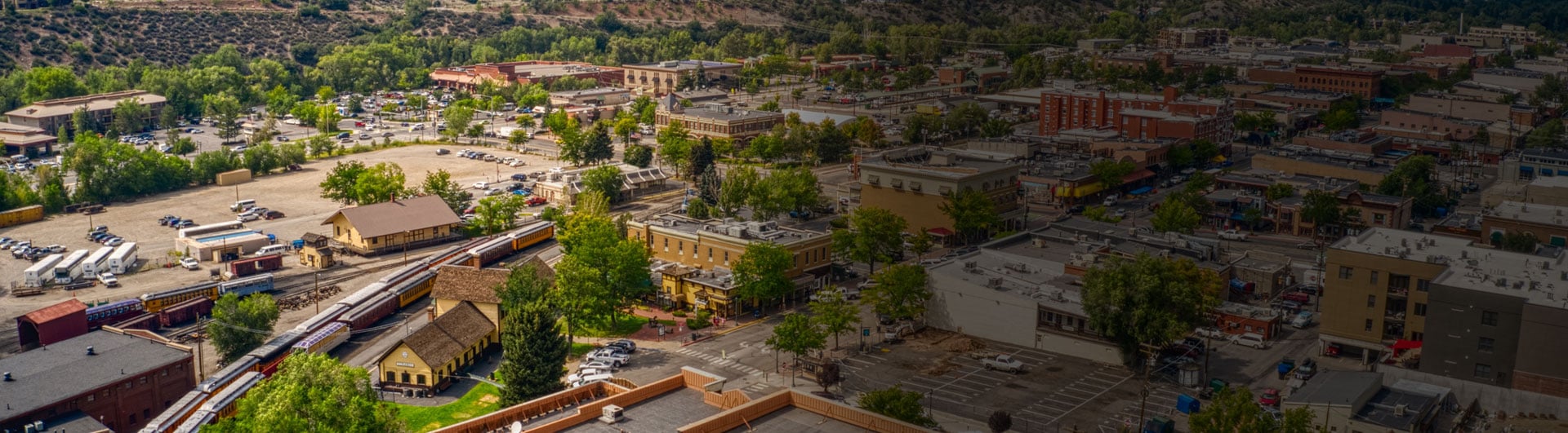 Aerial view of a bustling town with historic buildings, greenery, and railway station under a clear sky.