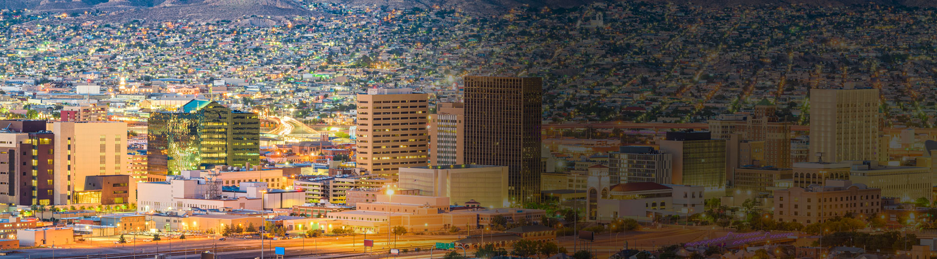 Colorful cityscape view at dusk with illuminated buildings and a sprawling urban landscape in the background.
