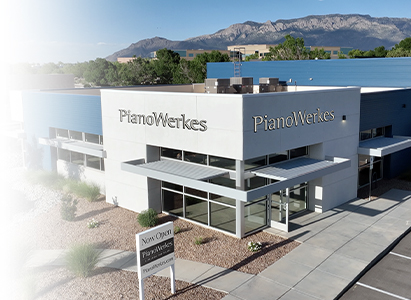 Exterior view of a modern PianoWerkes store with mountains in the background, showcasing the new location.