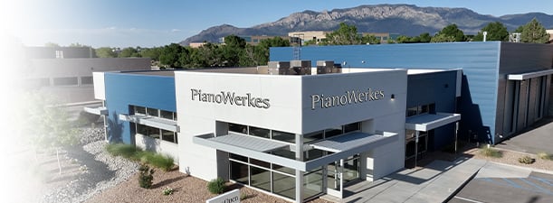 Modern PianoWerks building with mountain backdrop and clear blue sky.