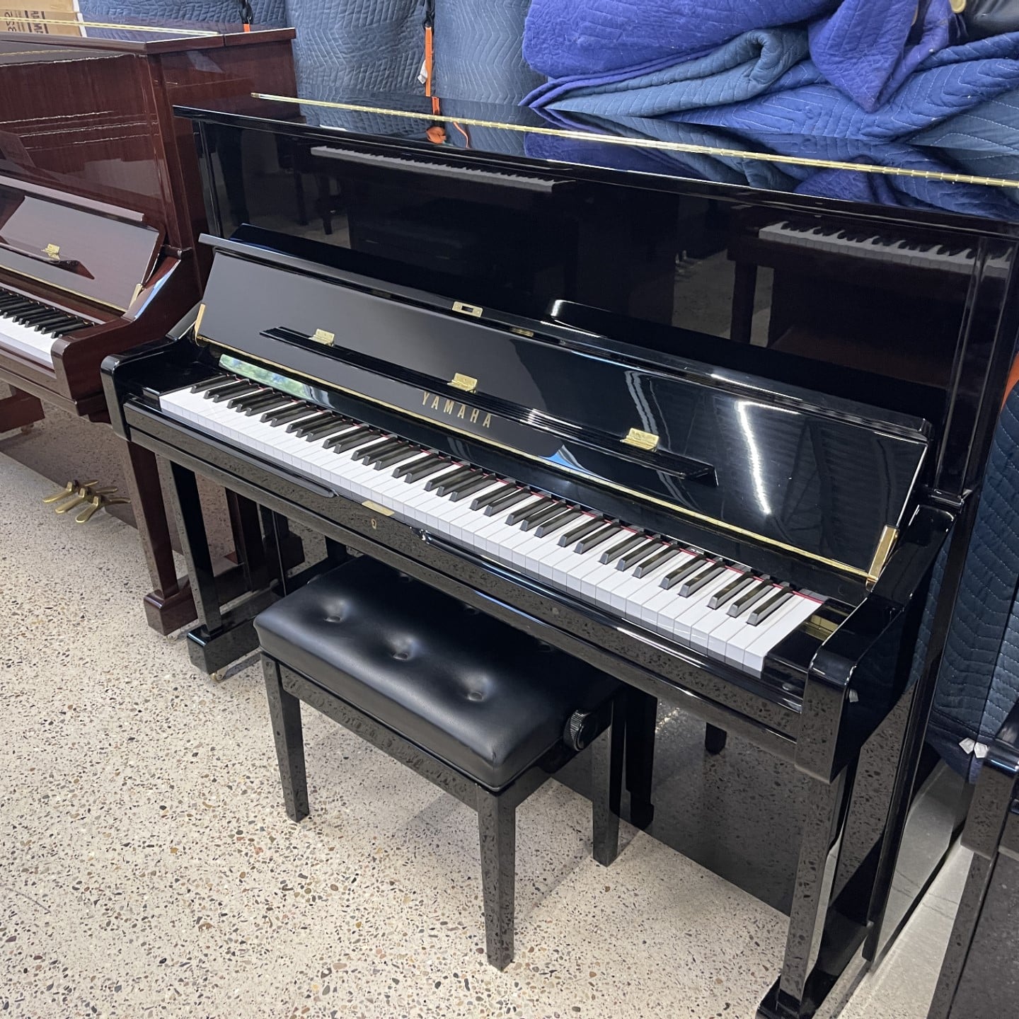 Black Yamaha upright piano with matching padded bench in a showroom setting.