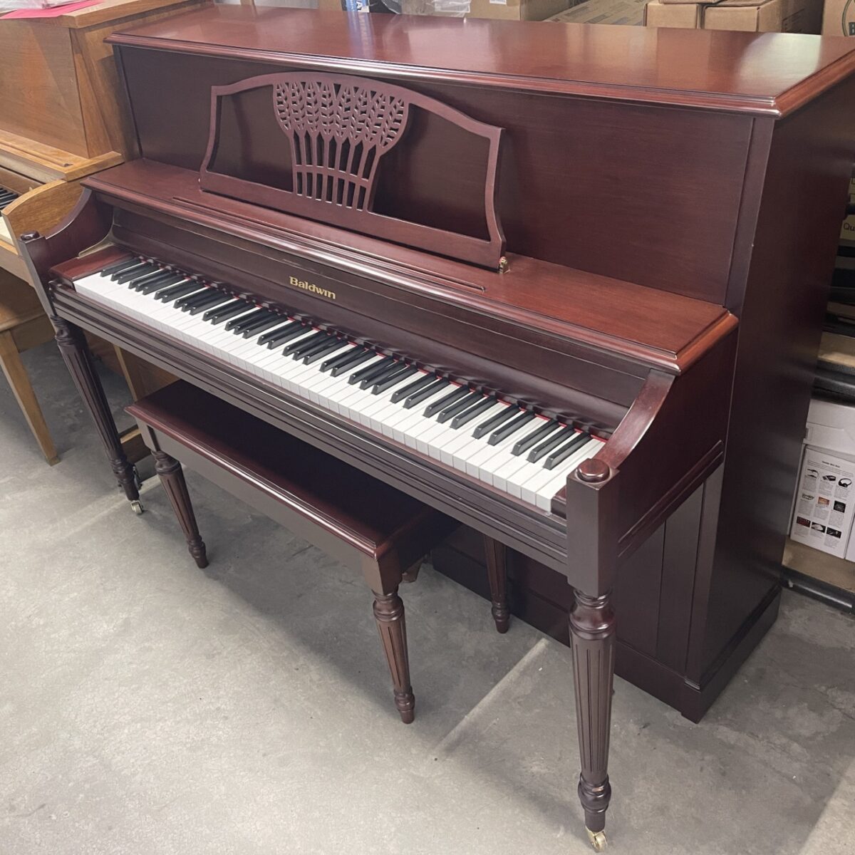 Classic Baldwin upright piano with mahogany finish and matching bench on display in a showroom.