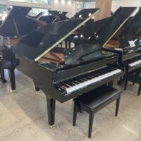Black grand piano in a showroom with others in the background, polished finish and open lid.