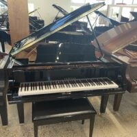 Black Yamaha grand piano on display in a showroom with other pianos in the background.