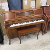 Wooden Yamaha upright piano with matching bench in warehouse setting. Ideal for music enthusiasts.