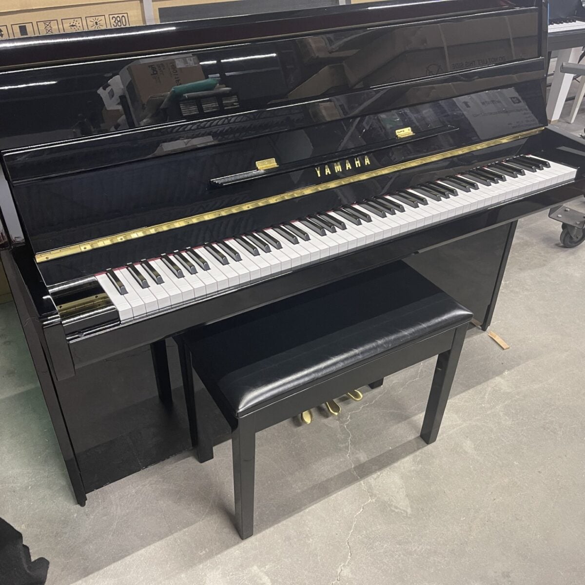 Black Yamaha upright piano with a matching bench on a concrete floor.