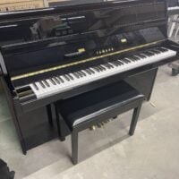 Black Yamaha upright piano with a matching bench on a concrete floor.