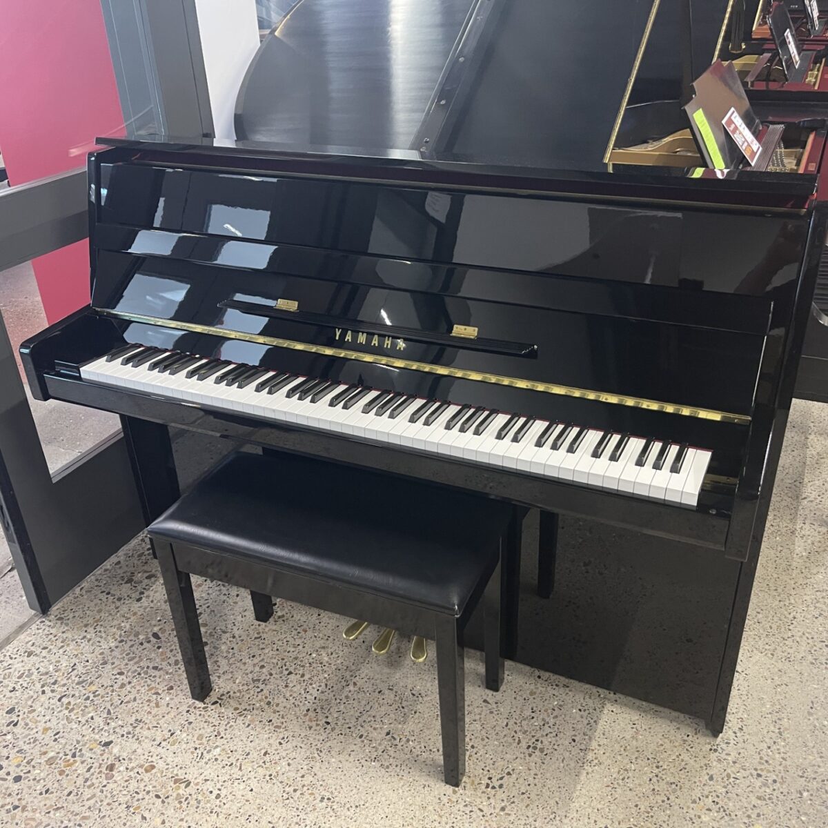 Black Yamaha upright piano with matching bench in a showroom setting.