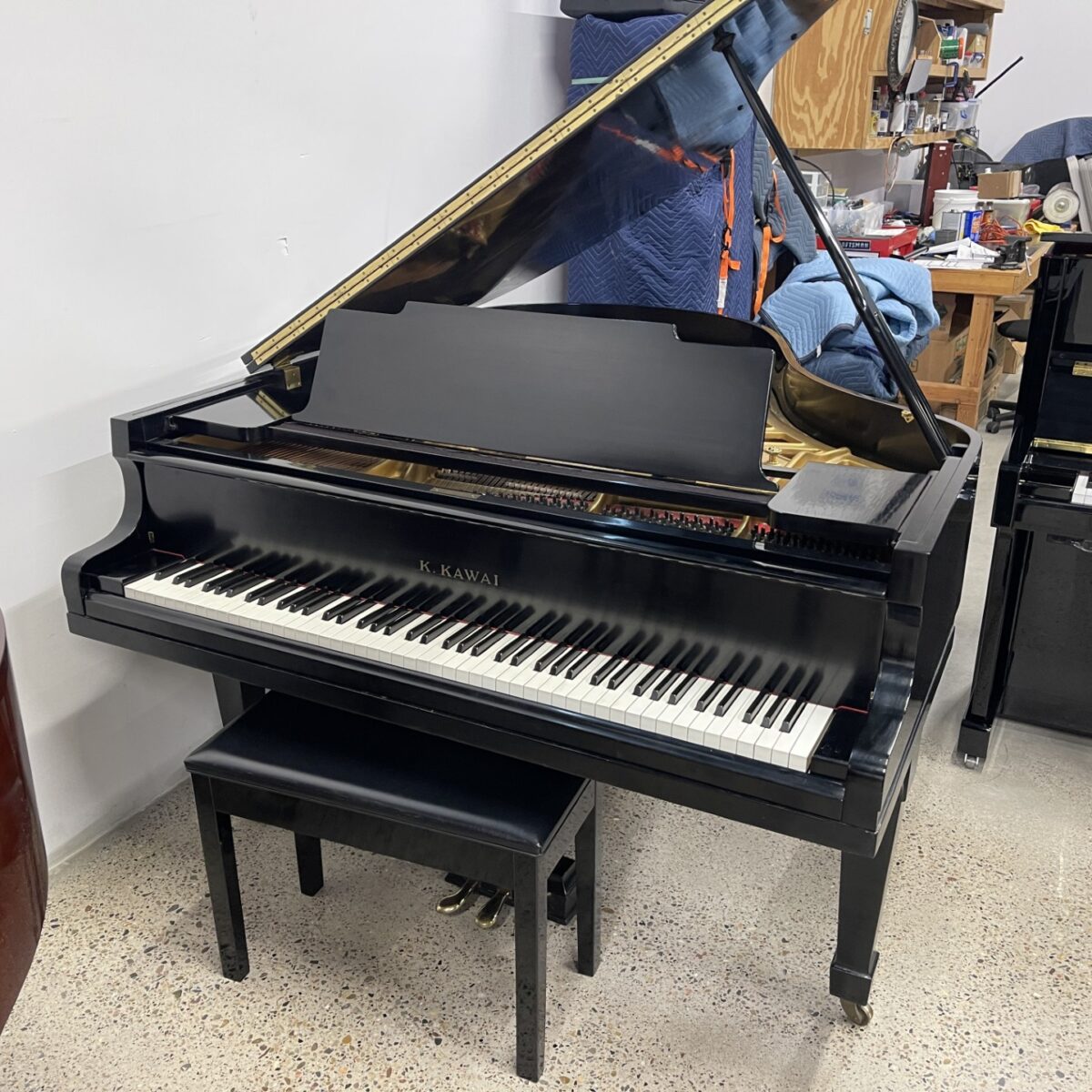 Black Kawai grand piano with open lid, placed in a workshop, showcasing its sleek design and detailed craftsmanship.