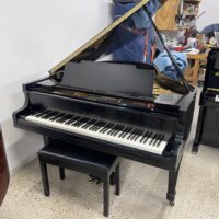 Black Kawai grand piano with open lid, placed in a workshop, showcasing its sleek design and detailed craftsmanship.