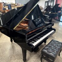 Black grand piano with open lid and bench in a showroom. Elegant instrument on a polished floor.