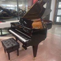 Elegant black grand piano with open lid and matching stool in a modern showroom.