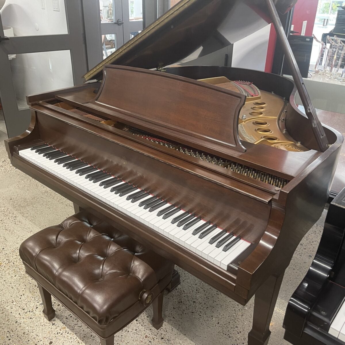 Elegant grand piano with open lid and cushioned bench in a showroom setting.