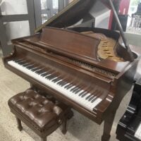 Elegant grand piano with open lid and cushioned bench in a showroom setting.