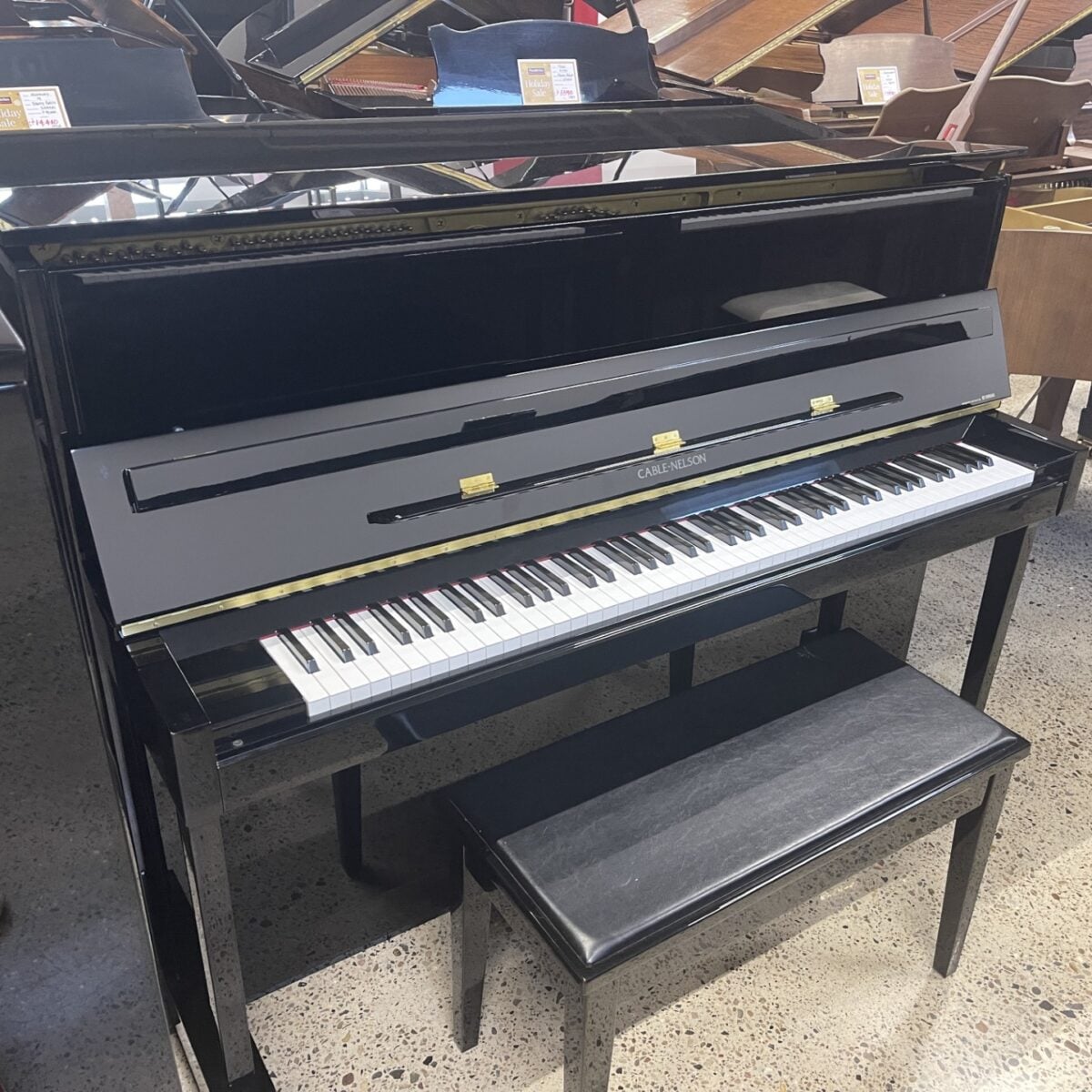 Black upright piano with bench in a showroom, featuring polished finish and open top. Perfect for music enthusiasts.