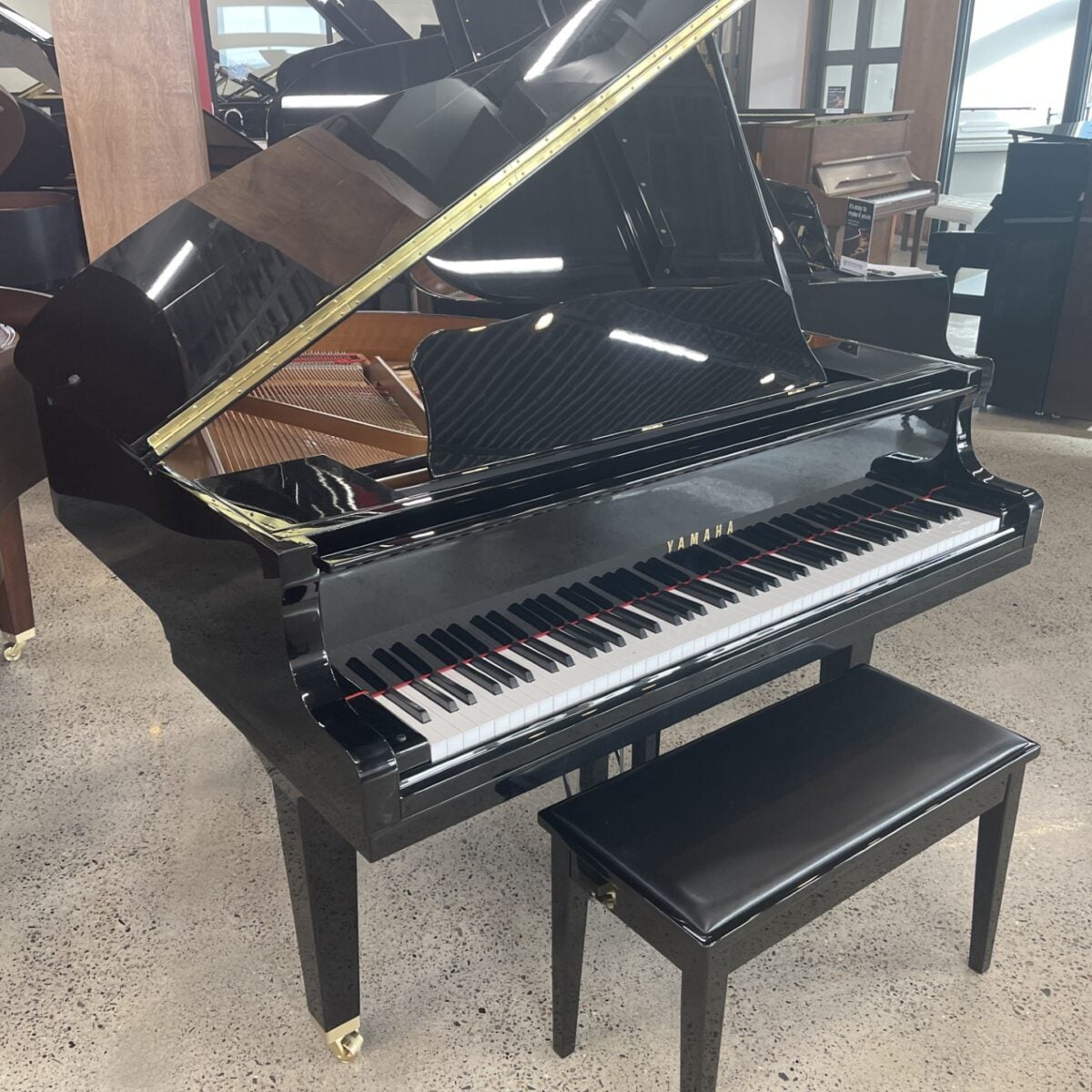 Luxury black grand piano with bench on a polished floor in a showroom setting.