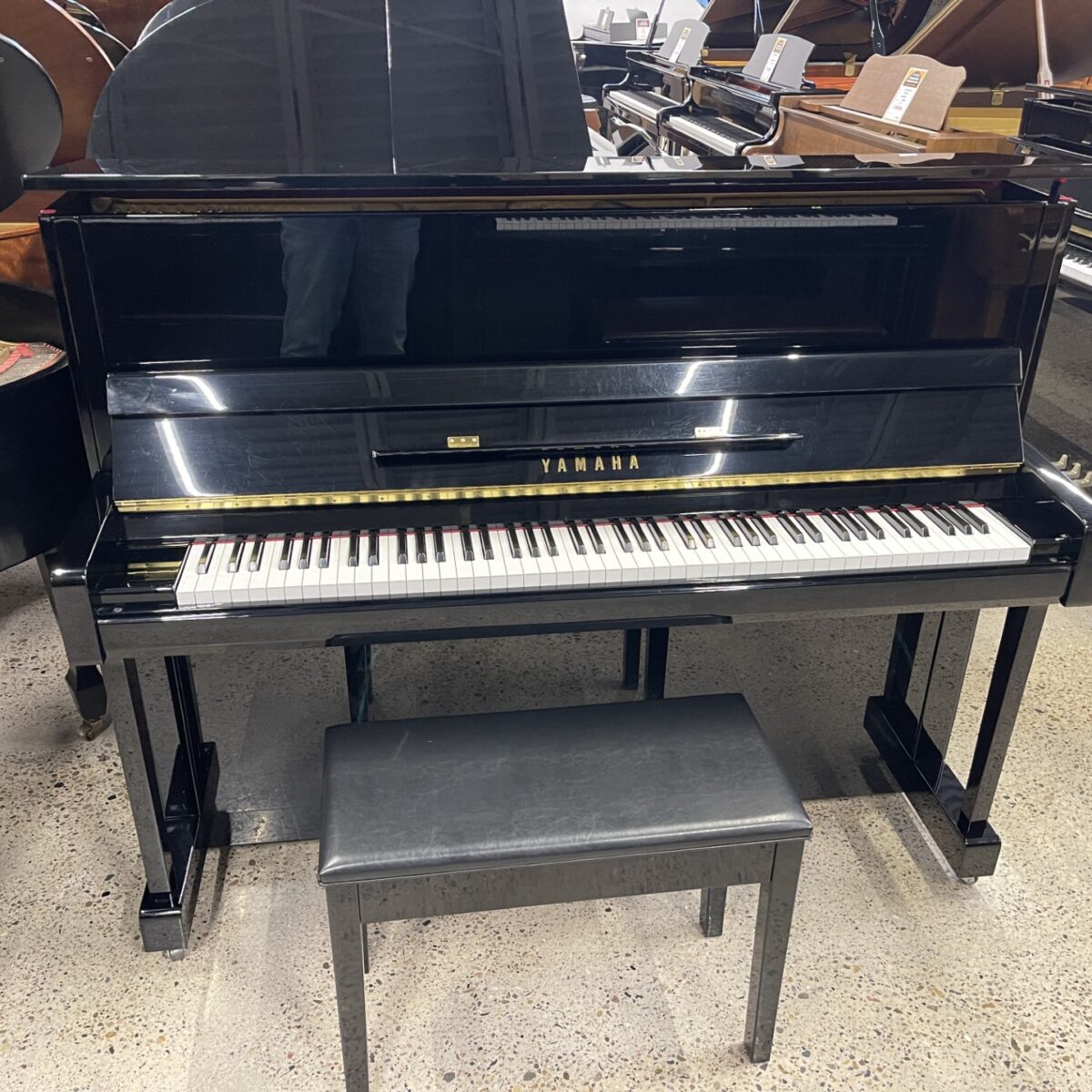 Black Yamaha upright piano with matching bench on showroom floor.