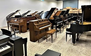 ClassicABQ-Showroom-UsedPianos Showroom filled with various pianos, both grand and upright, arranged in rows under bright lighting.