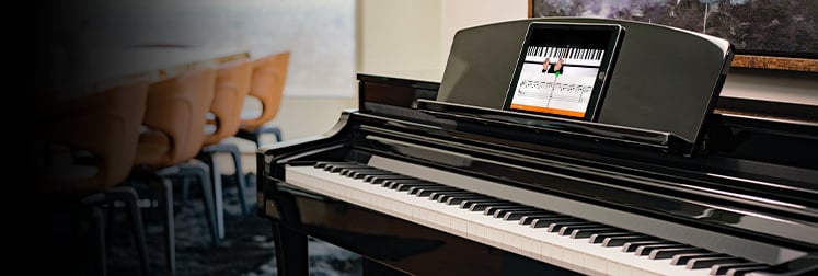Digital grand piano with a music app on screen, set in a modern room with a wooden dining table in the background.