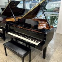 Black Yamaha grand piano with polished finish, open lid revealing interior. Located in a bright showroom setting.