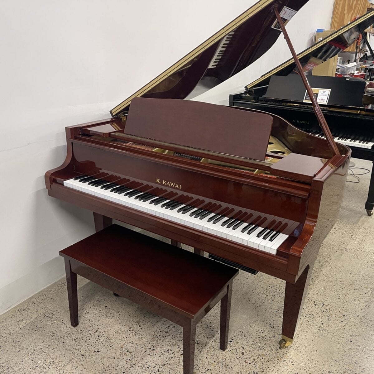 Alt text: K. Kawai polished mahogany grand piano with a matching bench, showcasing premium craftsmanship and rich sound quality.