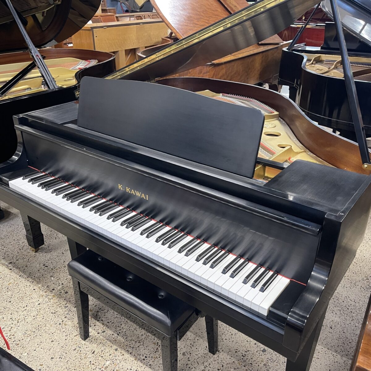 Alt text: Kawai upright piano featuring polished black finish and white keys, ideal for beginners and seasoned players.
