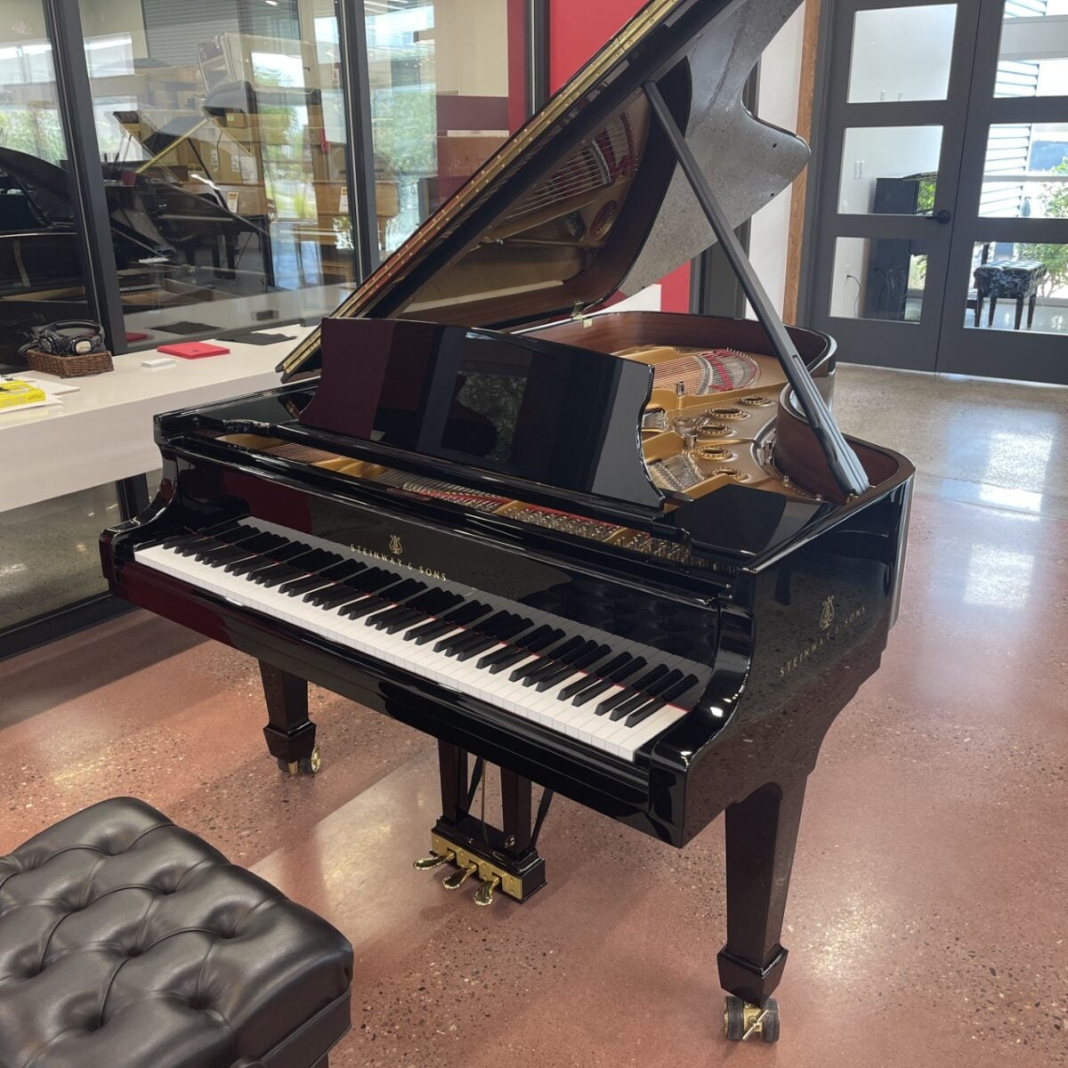Steinway & Sons grand piano with polished ebony finish, white keys, and brass pedals showcased in the Piano Werkes showroom.