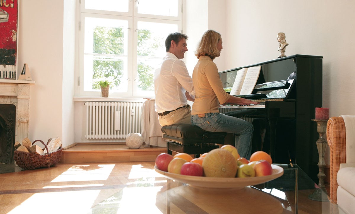 Couple enjoying a duet on a polished black upright piano, featuring a rich soundboard and elegant design at PianoWerks.