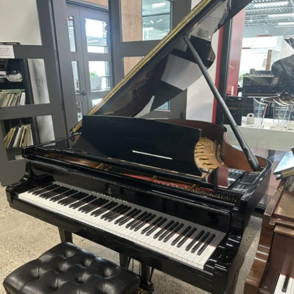 Polished black grand piano with intricate craftsmanship and a tufted leather bench, showcasing Yamaha’s finest design.