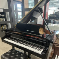 Polished black grand piano with intricate craftsmanship and a tufted leather bench, showcasing Yamaha’s finest design.