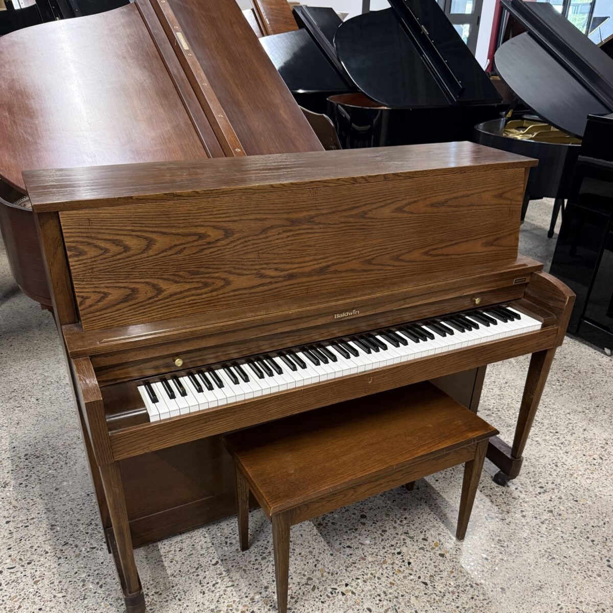 Baldwin upright piano in rich oak finish, featuring a sleek design and responsive keys, perfect for any musician's home.