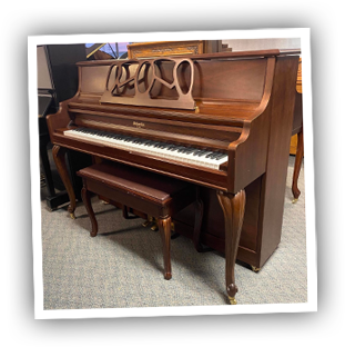 Wooden upright piano with ornate music stand and matching bench in a carpeted room.