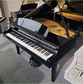 Black grand piano in showroom, open lid revealing strings and hammers, on gray carpet with another piano in the background.
