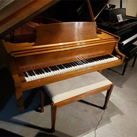 Wooden grand piano with matching bench on a gray floor, showcasing elegant design and craftsmanship.